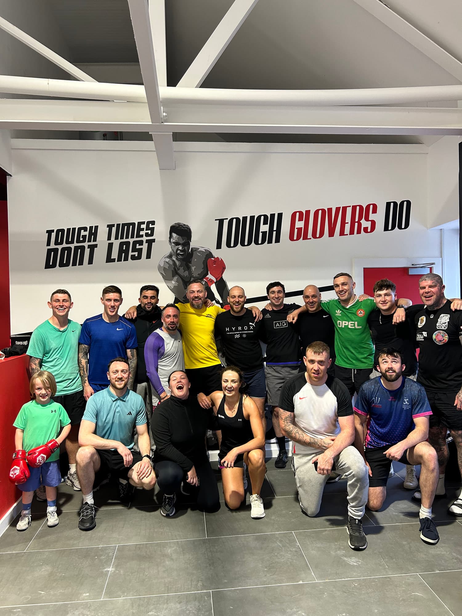 A group of Tough Glove members in front of the “Tough Times Don't Last, Tough Glovers Do” mural